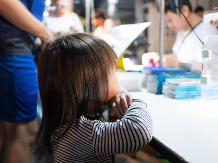 Lampang, Thailand; 5 October 2019 - Adorable Asian child girl stand to wait to buy foods at Kad Kong Ta Walking Street.のeditorial素材