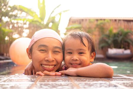 Happy mother and daughter playing in swimming pool at resort.