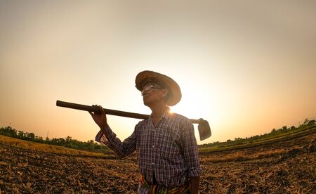 Elderly Asian farmers shoveling and prepare the soil with a spade for planting on sunset background.の写真素材
