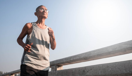 Asian senior man in sportswear jogging on bridge over sky background. Healthy lifestyle and...