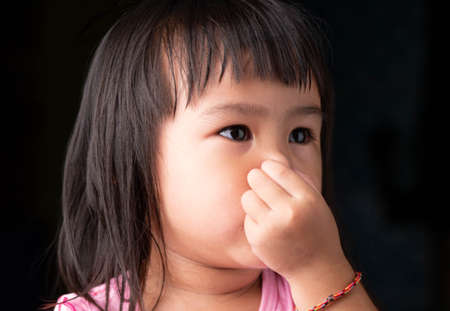 Portrait face of Asian little child girl holding her nose because of a bad smell on dark background.の写真素材