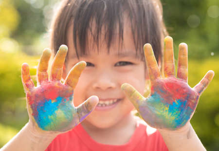 Cheerful little child girl with hands painted in colorful paints on nature background.の写真素材