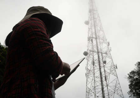 Female engineer using tablet computer checking the frequency with telecommunication towers with TV...