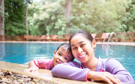Happy young mother and her daughter smiling in swimming pool in a hot summer day. Family lifestyle in vacation.の写真素材
