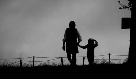 The silhouette of mother holding her daughter's hand walking on lawn in the park.の写真素材