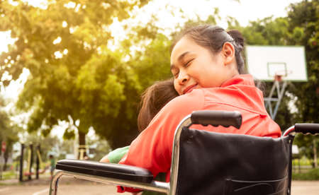 Happy mother in a wheelchair hugging little girl sitting on her lap in the park. Disabled, motherhood concept.の写真素材