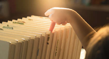A little cute girl is choosing a book in the bookshelves at home. Stay at home to quarantine from  pandemic. Homeschool concept.の写真素材