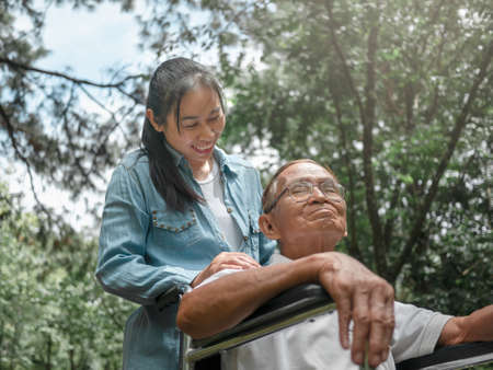 Grandfather in a wheelchair with granddaughter enjoying nature in the park. Family life on vacation.の写真素材