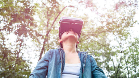 Happy woman wearing VR-headset glasses of virtual reality in forest and enjoying the nature on a...