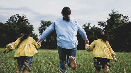 Mother and daughters holding hands and running on field in summer park. Happy family spend their free time together on vacation.の写真素材