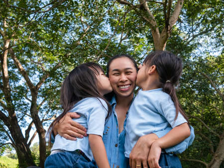 Two sibling little girls with mom laughing and hugging each other on warm and sunny summer day in...