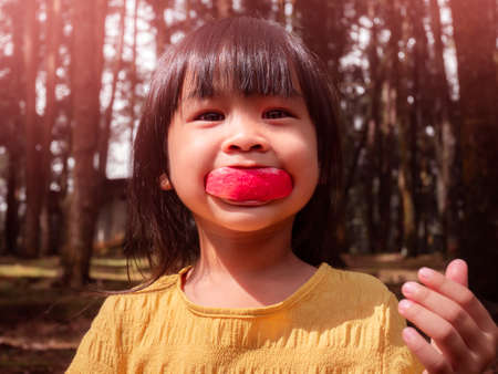 Portrait of happy little girl eating red apple outdoors in summer. Childhood happiness.の写真素材