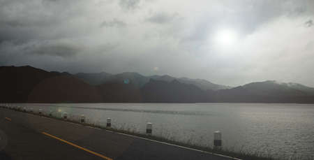 The view of empty asphalt road and natural landscape of evening lake on rainy season cloudy sky background.の写真素材