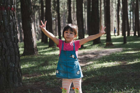 Active little girls running in the pine forest on a warm summer day. Happy girl smiles and laughs while spending time with her family in the park on vacation.の写真素材