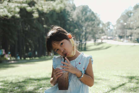 Cute little girl drinking delicious iced chocolate or cocoa in the summer outdoor garden. Family having a picnic in the park.の写真素材