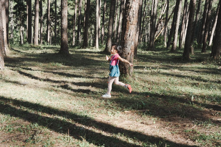 Active little girls running in the pine forest on a warm summer day. Happy girl smiles and laughs while spending time with her family in the park on vacation.の写真素材
