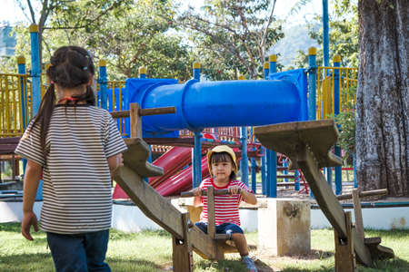 Active little sisters playing on a seesaw in the outdoor playground. Happy child girls smiling and...