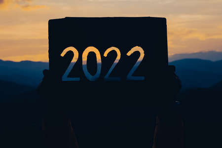 Hands holding of new year 2022 silhouette design from cardboard against the background of mountain with sunset. Happy New Year concept.の写真素材