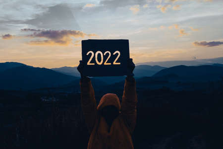 Hands holding of new year 2022 silhouette design from cardboard against the background of mountain with sunset. Happy New Year concept.の写真素材