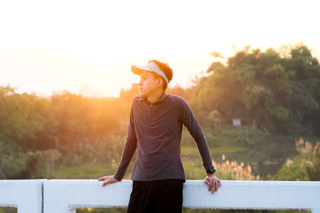 A healthy teenage boy resting on a bridge after jogging in the morning. Young man exercising outdoors.の写真素材