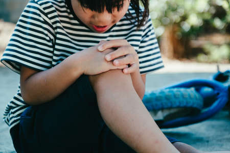 Sad little girl sitting on the ground after falling off her bike at summer park. Child was injured while riding a bicycle.の写真素材