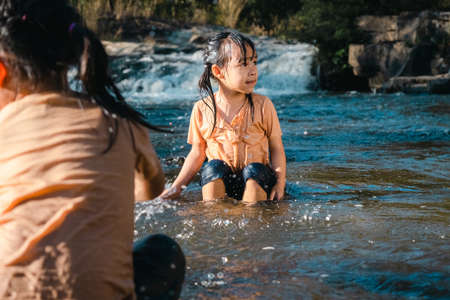 Asian little girl playing in the forest stream with her sister. Active recreation with children on river in summer.の写真素材