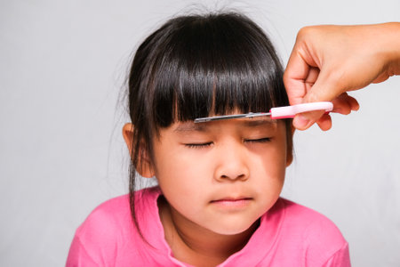 Asian mother cuts her daughter's hair by herself at home. Mom cuts hair for a cute little girl. Stay home safe from corona virus Covid-19の写真素材