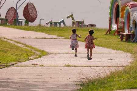 Rear view of children running on the road in the park. Two cute sisters are playing in the summer...