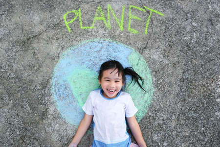 Cute little girl lying on a beautiful world painting with chalk labeled Planet on asphalt. Young...
