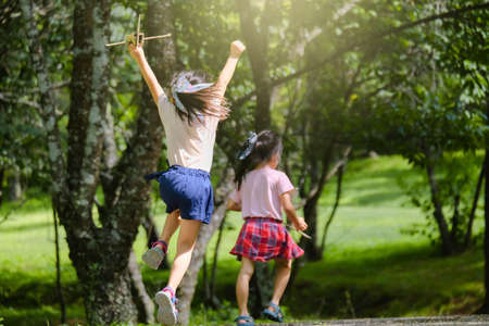 Happy children playing with cardboard planes in the summer garden. Two little sisters with toy...