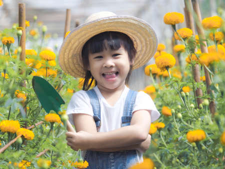 Cute little girl in hat holding garden tool shovel for planting flowers in the garden. A child helps mom in the garden, a little gardener.の写真素材