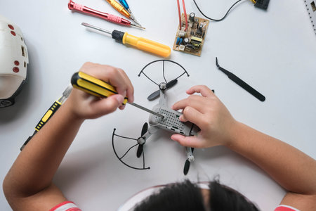 Concentrated little girl repairing her toy drone with a tool in hand and carefully assembles toy...