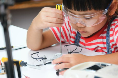 Concentrated little girl repairing her toy drone with a tool in hand and carefully assembles toy drone with screwdriver. STEM Hobbies for advanced smart kids.の写真素材