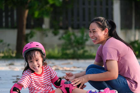 Asian mother helps daughter practice roller skating in the park. Exciting outdoor activities for kids.の写真素材
