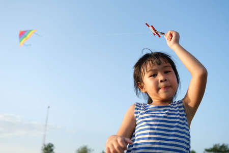 Child playing with a kite while running on a meadow by the lake at sunset. Healthy summer activity for children. Funny time with family.の写真素材