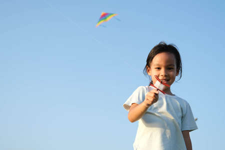 Child playing with a kite while running on a meadow by the lake at sunset. Healthy summer activity for children. Funny time with family.の写真素材