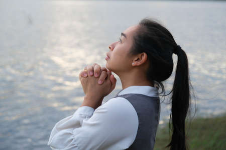 Woman praying alone at sunset. Woman pray for god blessing to wishing have a better life. Spiritual and religion concept.の写真素材