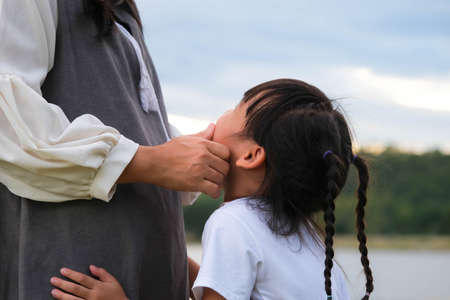 Loving mother touching the face of a cute smiling girl having fun together by the lake. Happy family, mother and little daughter playing feeling happy in the park.の写真素材