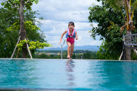 Little girl in a life jacket jumps into an outdoor swimming pool. Cute little girl playing in the pool on a sunny day. Summer lifestyle concept.の写真素材