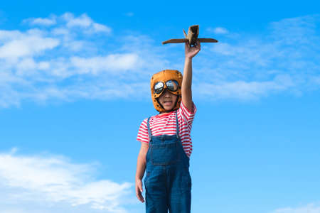 Cute little girl running through the meadow on a sunny day with a toy plane in hand. Happy kid playing with cardboard plane against blue summer sky background. Childhood dream imagination concept.の写真素材