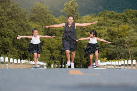 Two lovely daughters are running with their mother spreading their arms as if flying on the road in...