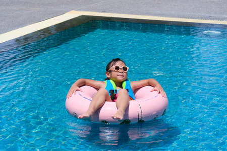 Little girl in a swimsuit relaxing on the inflatable ring in pool. Cute little girl playing in the...