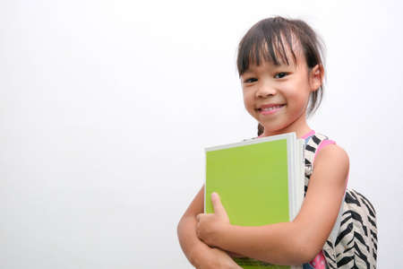 Back to school. Smiling little girl carrying a backpack holding books looking at the camera on a...