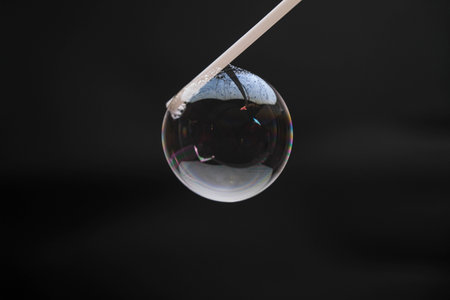Beautiful soap bubbles are blown with a straw on a black background. Abstract soap bubbles with...