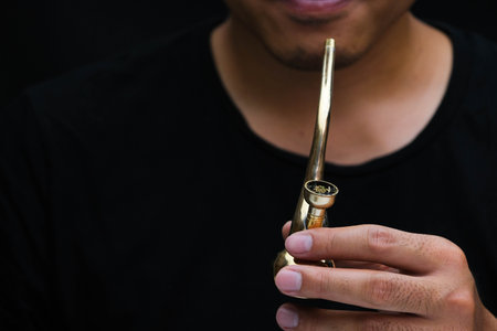 Asian man smokes marijuana from a pipe at home. Studio shoot with model simulating smoking pot with...