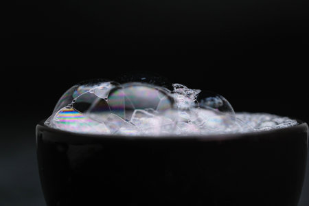 Black cup with foam water and bubbles on black background. Soap bubbles in motion background.
