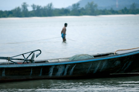 Thai small fishing boat moored on the beach with fishermen preparing to go fishing in the morning in the background. Life in the traditional Thai countryside.の写真素材