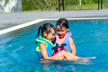Happy little sisters play in outdoor swimming pool of tropical resort during family summer vacation. Kids learning to swim. Healthy Summer Activities for Kids.の写真素材