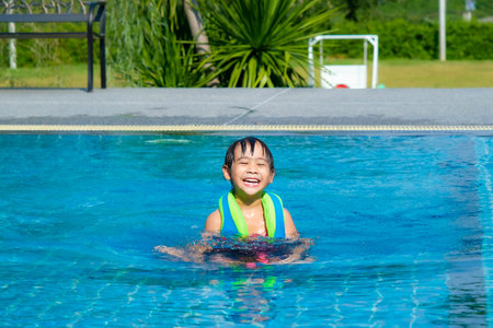 Little girl plays in the outdoor swimming pool of tropical resort during family summer vacation. Kids learning to swim. Healthy Summer Activities for Kids.の写真素材