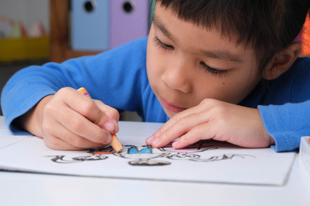 Cheerful happy little girl drawing with crayons on paper sitting at table in her room at home. Creativity and development of fine motor skills.の写真素材